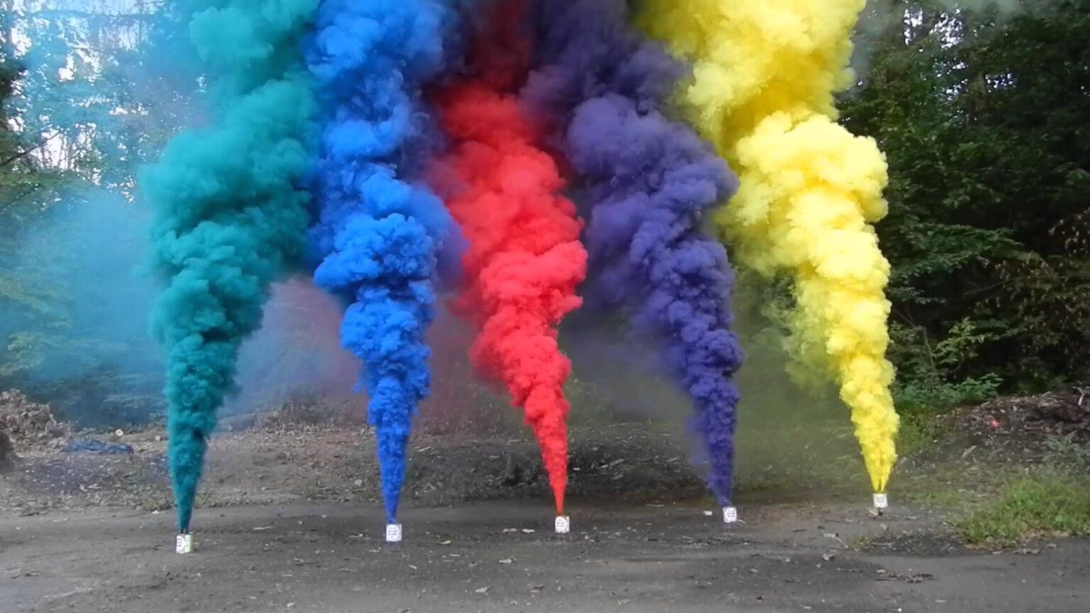 Five colored smoke grenades releasing tall plumes of teal, blue, red, purple, and yellow smoke on a paved outdoor surface, dramatic and vibrant